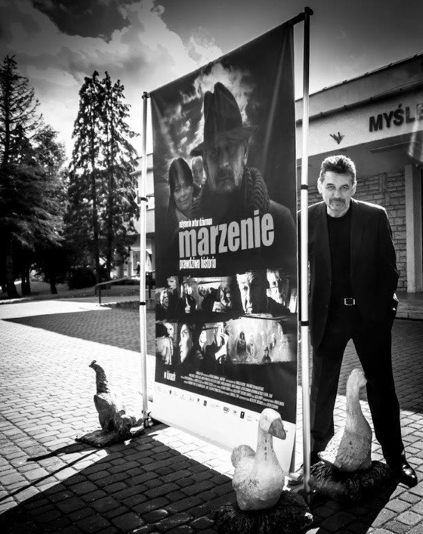 Artur Dziurman, reżyser filmu stoi przy plakacie filmu "Marzenie" przed Myślenickim Ośrodkiem Kultury i Sportu