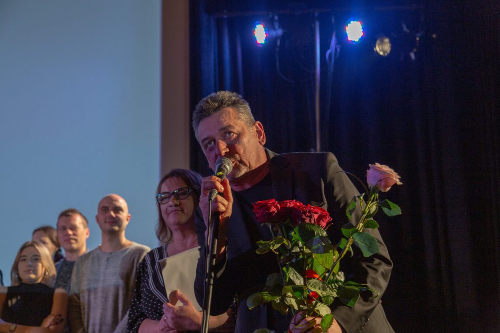 Artur Dziurman na premierze. Trzyma kwiaty w tle aktorzy teatru ITAN.
