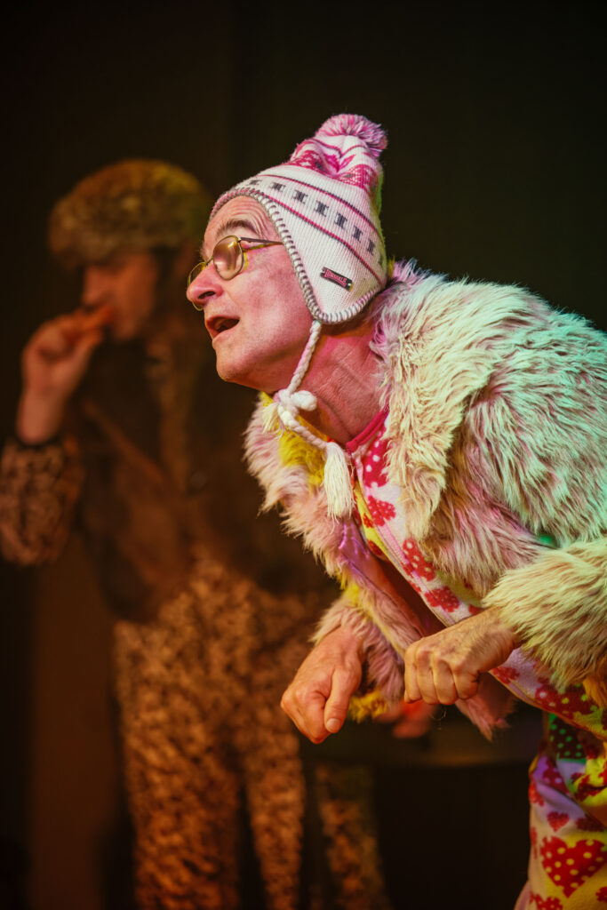 Aktor Jan w stroju Susła oraz w tle aktor Mietek w stroju Szaraka jedzącego marchewkę w trakcie spektaklu.