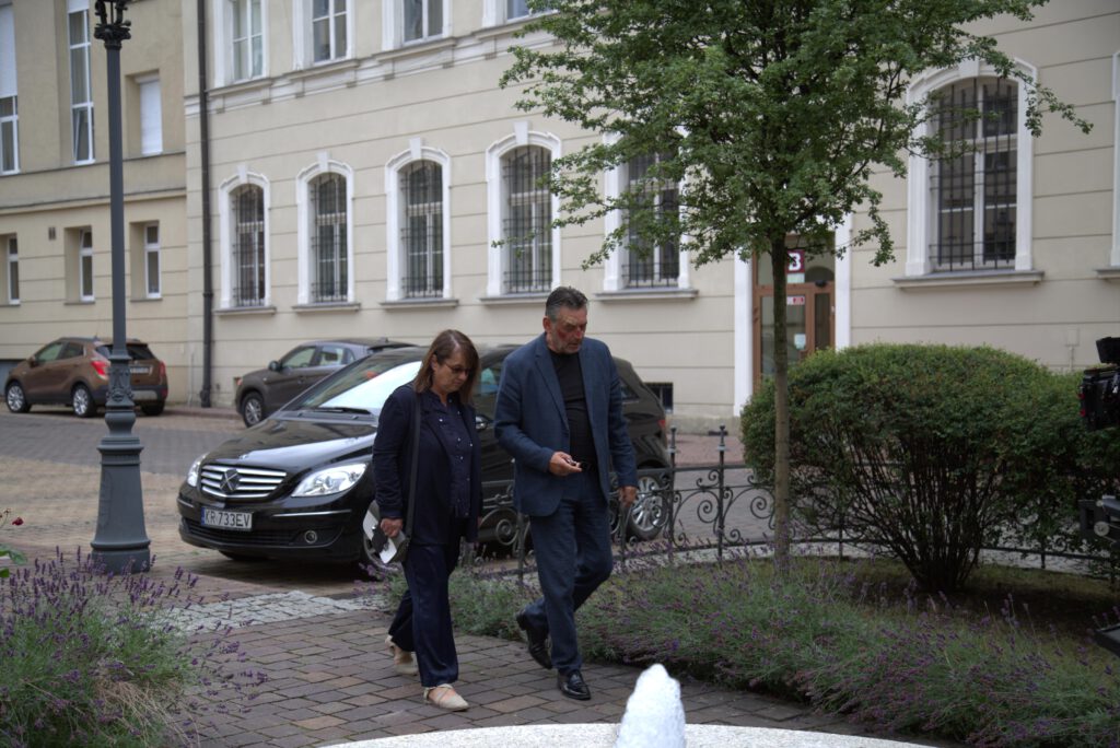Kadr z serialu; reżyser Artur i dyrektorka Danusia elegancko ubrani idą do gabinetu marszałka.