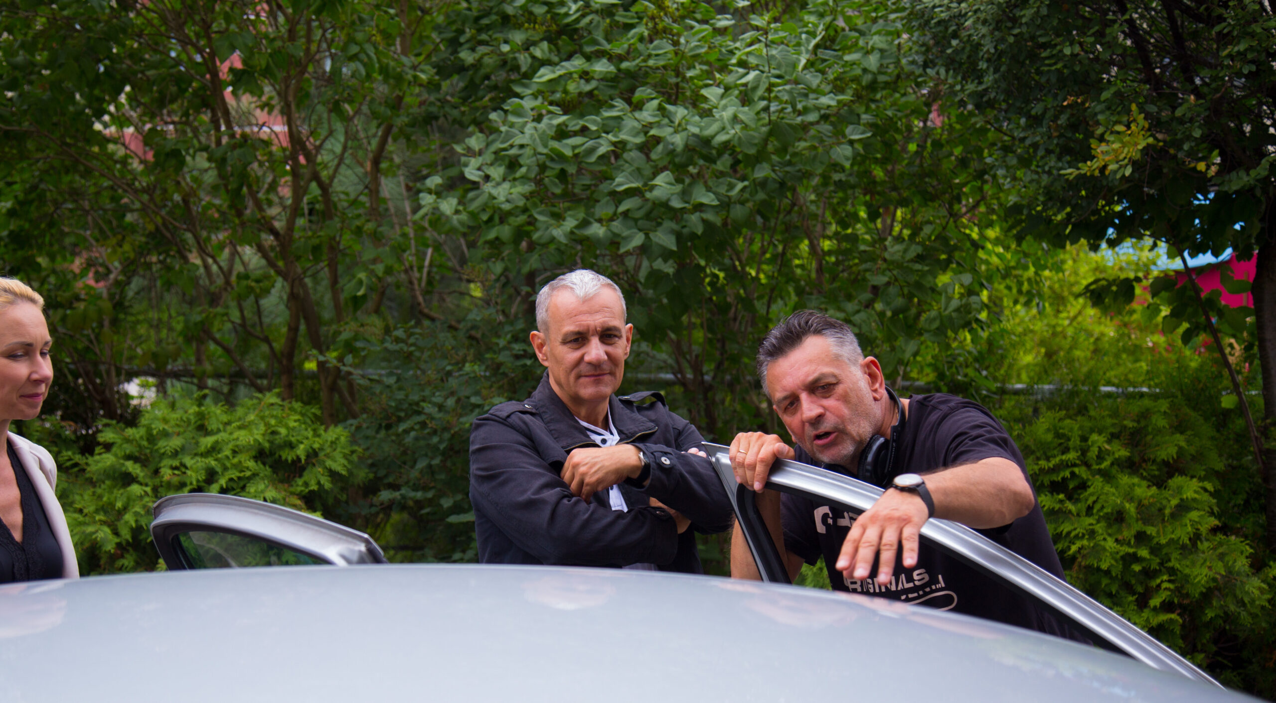 Reżyser Artur wraz z aktorem Maciejem Jackowskim ustawiają scenę przy srebrnym samochodzie.