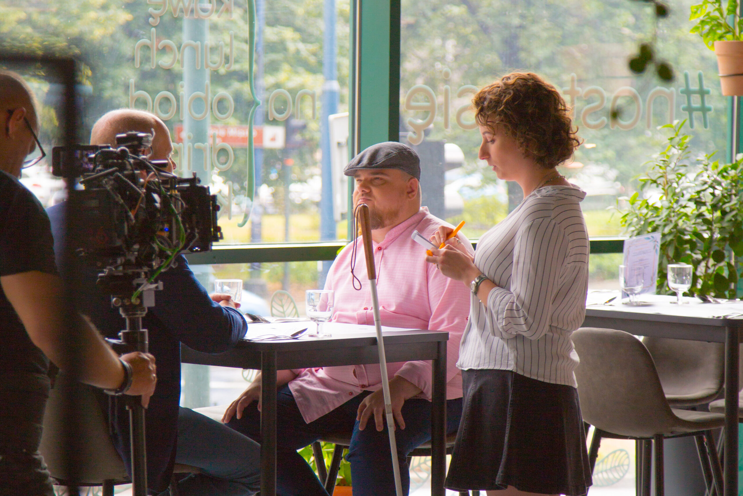 Aktorzy Jan i Michał siedzący przy stoliku w restauracji. Rozmawiają z aktorką Gabrielą, w roli kelnerki.