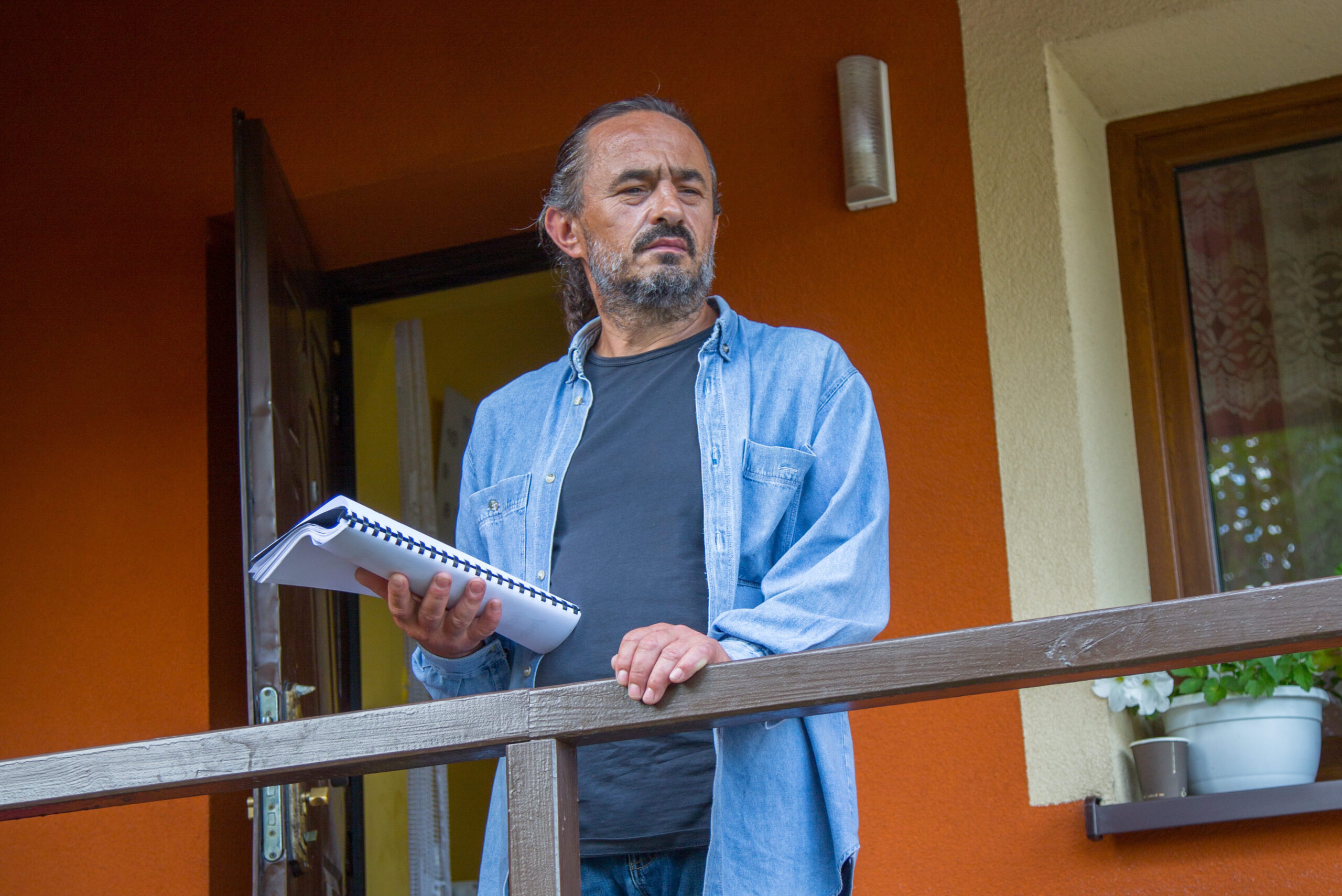 Aktor Mietek na werandzie swojego domu. W ręce trzyma scenariusz, spogląda ponad obiektyw.