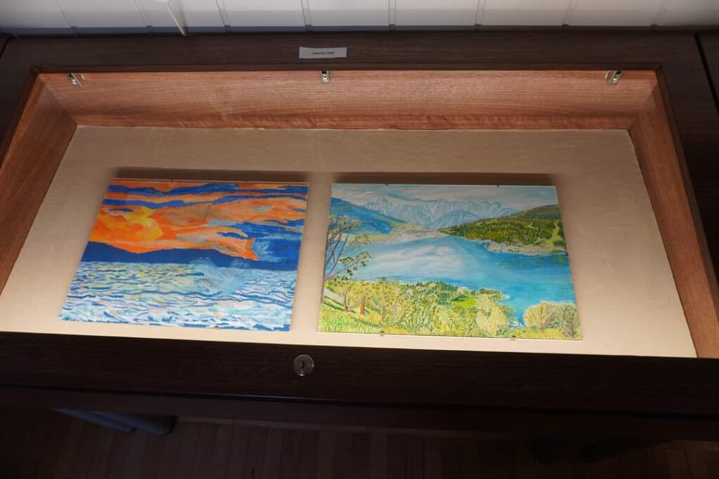 Szklana gablota będąca częścią wystawy. W niej dwa malunki: po lewej przedstawiający wzburzone morze, po prawej górskie jezioro.